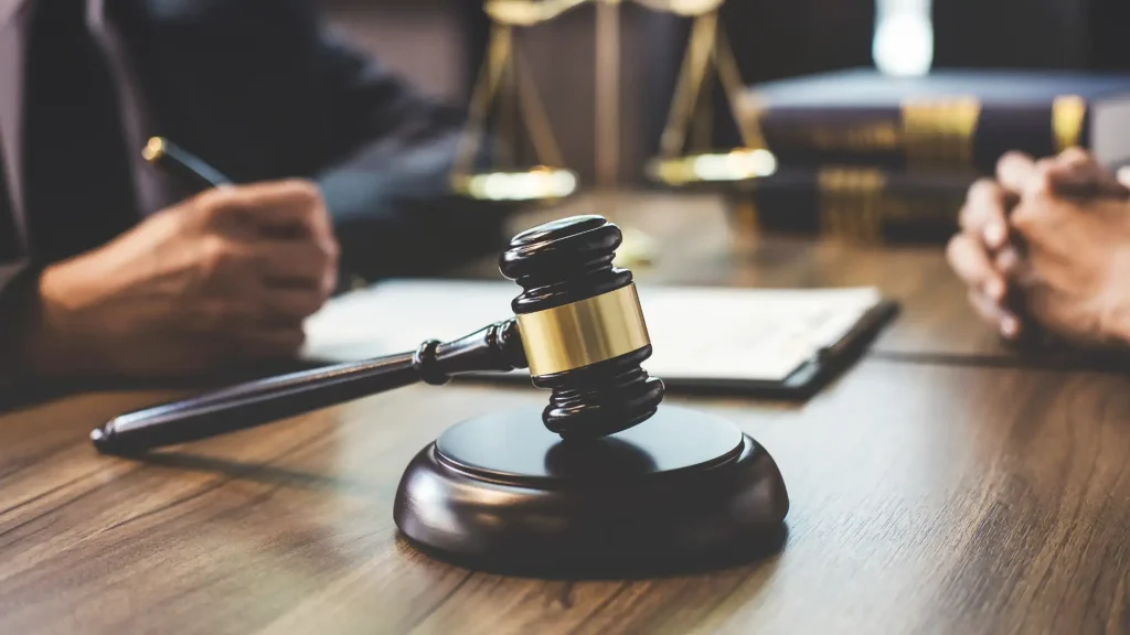 A gavel on a wooden desk, with legal documents and scales of justice in the background