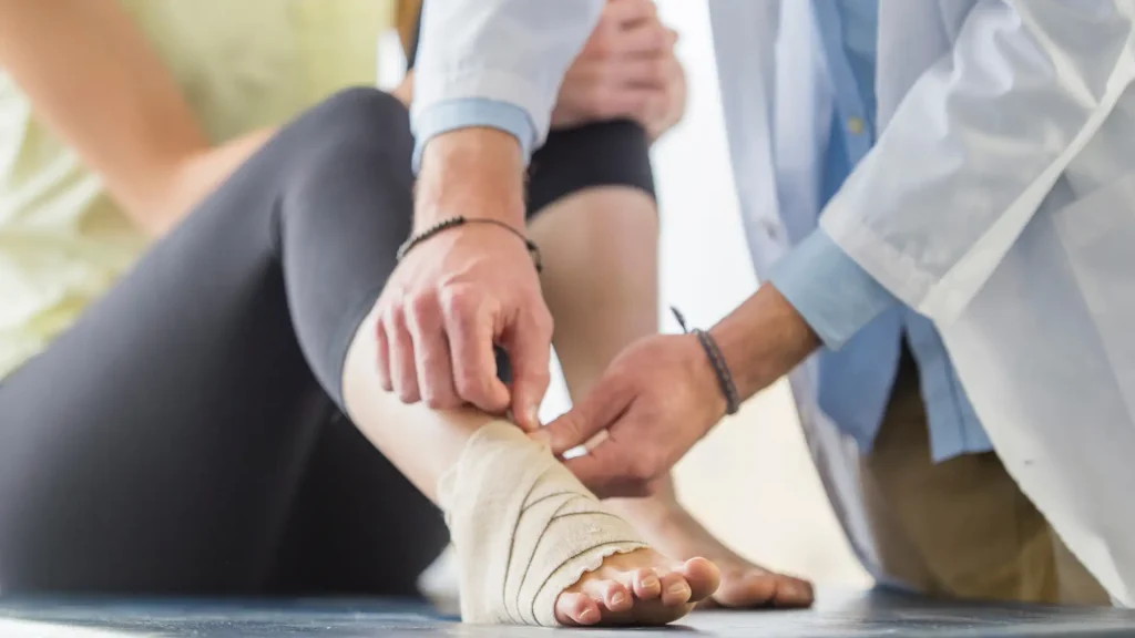 A medical professional wrapping a bandage around an injured ankle.