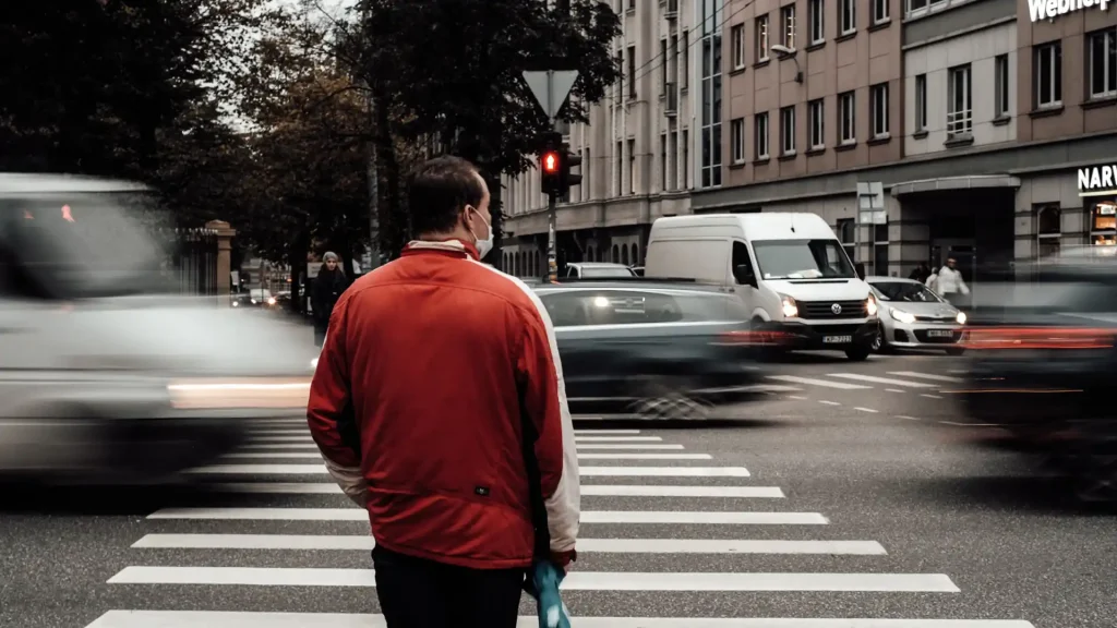 Person standing at a crosswalk with traffic moving in the background.