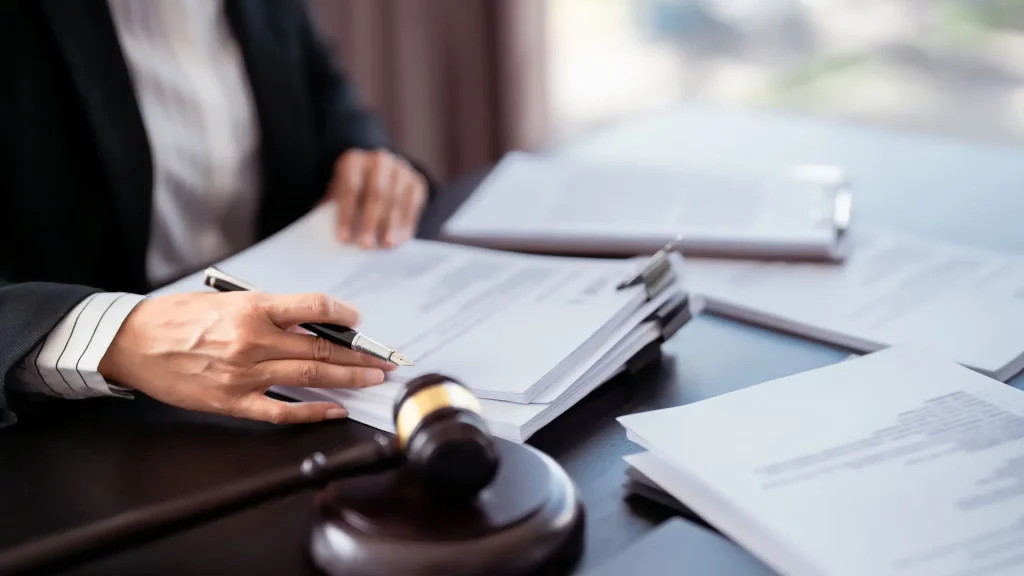 Close-up of a hand signing legal documents with a gavel in the foreground.